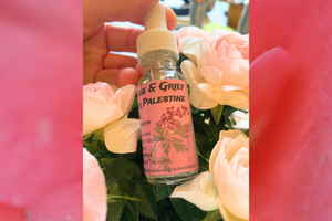 photo of a hand holding a tincture bottle next to pink roses. The label of the bottle is also pink with text and the image of a bleeding heart flower on a rose petal background