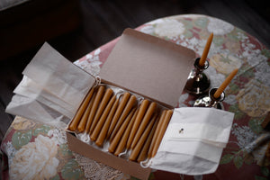 A box of many pairs of beeswax candles is displayed on a table
