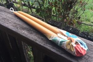 Two 10 inch beeswax candles laying down, bottom part tied with a multicolor cloth
