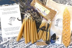 an offering of golden beeswax candles in different shapes and sizes alongside poetry offerings and herbs on a table