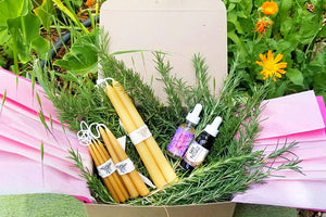 a summer heart of fire creative ritual box in the garden contains one pair of 10" taper candles, 2 pairs of 6" candles, , 4 pairs of mini candles, a bottle of Molten Courage, a bottle of Safe Passage and fresh sprigs of rosemary