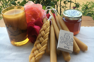 a grouping of different kinds of candles, a jar of honey, a box of matches and roses on a table