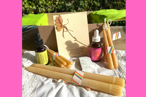 image of a box with braided and tapered candles next to a tincture bottle, ,matches, and a piece of writing