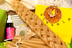 photo of a box with braided and tapered candles next to a tincture bottle, and some paper with writing