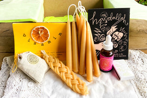 image of a box with braided and tapered candles next to a tincture bottle, ,matches, a satchel with a stamp and a "havdallah" book