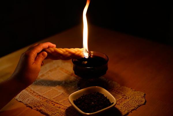 braided candle aflame held above a goblet and a dish on a lace doily