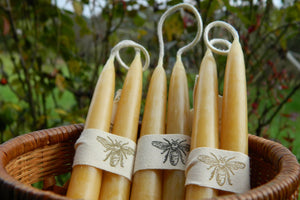 three pairs of candles tied with bee ribbon in a basket outdoors
